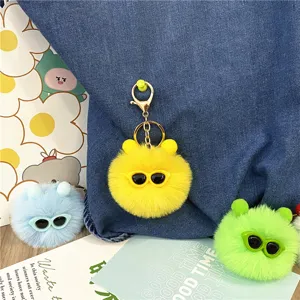 Macro view of colorful fuzzy monster ball keychains with sunglasses on denim bag