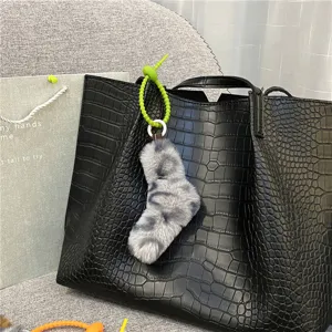 Detailed view of a soft leopard print plush sock charm hanging on a black crocodile tote bag