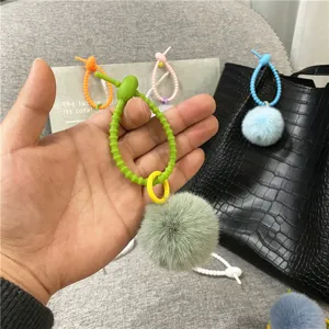 Hand holding a green plush pom-pom keychain bag charm with a wavy silicone cord detail.