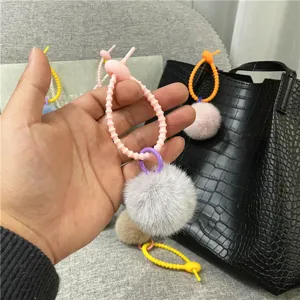 Close-up detail of a candy color plush pom pom bag charm attached to a black handbag