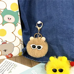 Macro view of cute brown plush pom-pom keychain featuring white sunglasses and gold clasp