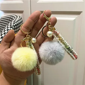 Detail of plush fur ball keychains with tweed straps and pearl charms in hand.