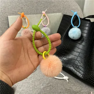 Close-up of a colorful silicone strap with a soft peach plush pom-pom bag pendant.