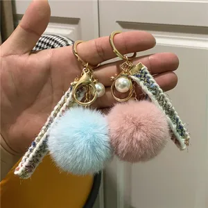 Detailed view of pink and blue plush pom-pom keychains with tweed ribbons and pearls