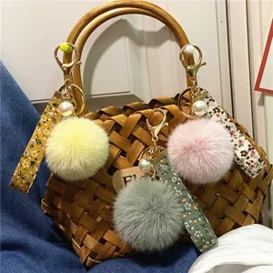 Floral strap pom-pom keychains with pearls shown on a woven bag
