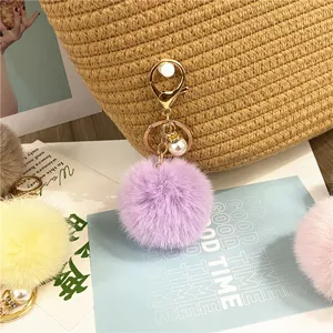 Close-up of a soft purple plush pom pom keychain with pearl charm on a straw bag