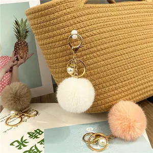 Close-up of soft pompom keychains with pearls and gold clips for bag decor.