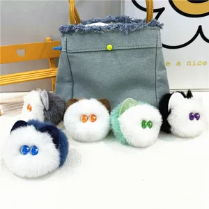 Collection of five colorful plush cat head charms displayed in front of a denim bag