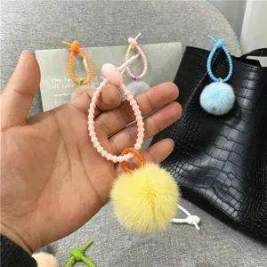 Detailed view of a pink silicone loop and yellow plush ball bag charm held in hand.