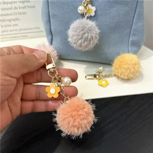 Detail of a fluffy pompom keychain with an enamel daisy flower and faux pearl charm.