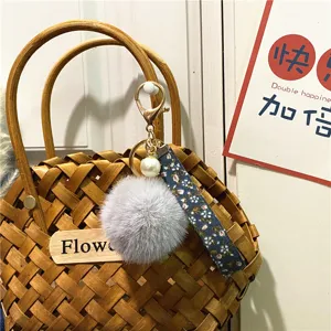 Detailed view of a cute floral strap keychain with a grey plush pompom and pearl