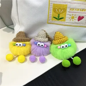 Detailed view of three colorful fuzzy monster plush keychains with hats on a white bag
