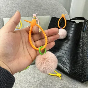 Detail view of a cute pink plush pom-pom keychain featuring a colorful orange silicone strap charm