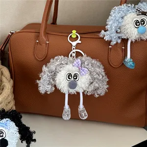 Close-up of a cute curly grey plush doll keychain hanging on a brown leather bag.