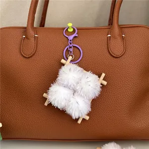 Close-up of fuzzy fermented bean curd keychain on a brown leather bag accessory.