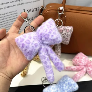 Macro view of a soft purple leopard print plush bow keychain bag charm held in hand