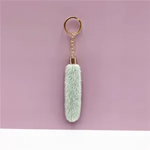 Close-up of mint green faux fur keychain with gold ring on mauve background