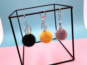 Three colorful faux fur pom pom keychains displayed on a minimalist black metal frame