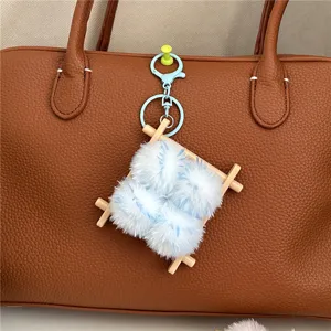 Detail view of a cute fuzzy pom-pom keychain attached to a brown leather handbag