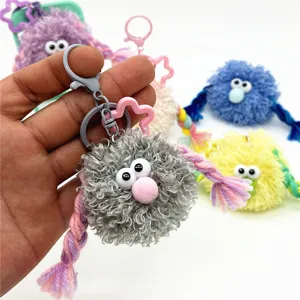 Detail of cute grey plush monster keychain with braided arms and large eyes