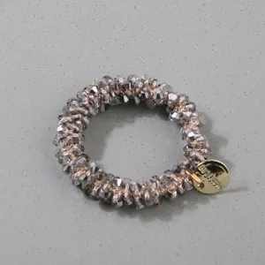 Detail of handmade grey crystal hair ring with a decorative gold-tone brand tag.