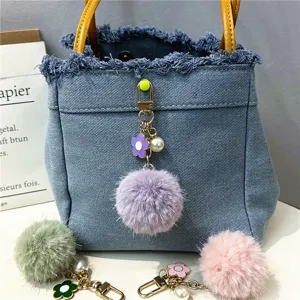Close-up of a purple flower pom-pom keychain with a pearl charm hanging on a denim bag