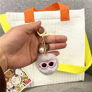 Close-up of a cute gray plush monster pom-pom keychain with stylish pink sunglasses