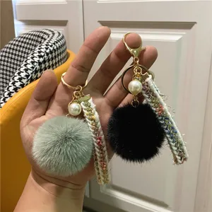 Close-up of elegant plush fur ball keychains featuring faux pearls and woven ribbons