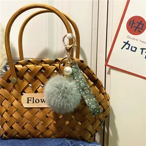 Detailed view of a floral strap keychain with grey pom-pom and pearl on a woven bag.