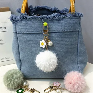 Close-up of cute white fur ball keychain with flower and pearl details on denim bag