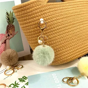 Close-up of mint green plush pom pom keychain with pearl accent on a woven bag