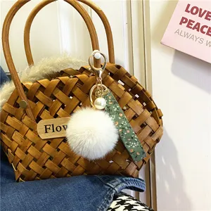 Detail view of a cute floral ribbon keychain with white fur pom-pom on a woven basket bag