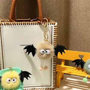 Close-up detail of cute furry bat monster plush keychain hanging on a stylish white bag