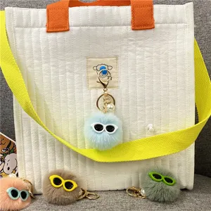 Close-up of cute plush monster pom-pom keychain with glasses on a white quilted bag