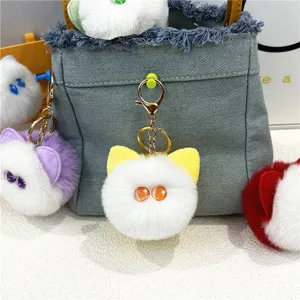 Detailed view of a white plush cat head keychain with big orange eyes on a denim bag