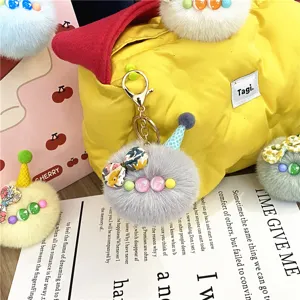 Detailed macro view of a cute gray plush pom pom doll keychain hanging on a yellow bag