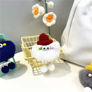 Close-up of white fluffy monster keychain with red knitted hat and big eyes on bag