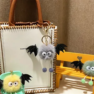 Close-up of cute grey fluffy monster keychain with bat wings and googly eyes