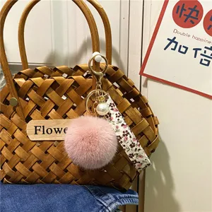Detailed view of pink fur pom-pom keychain with floral strap and elegant white pearl.