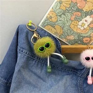 Close-up of cute fuzzy ball keychain with sunglasses and little boots on denim.