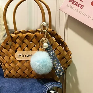 Close-up of floral ribbon keychain with light blue pompom and pearl charm on bag