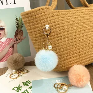 Close-up of pastel faux fur pom-pom keychain with pearl on a woven bag