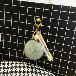 Detail of a green pom-pom keychain featuring a colorful ribbon and pearl accent