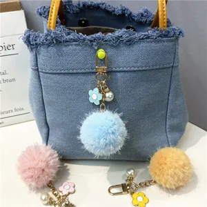 Detailed view of colorful pompom bag charms with flowers and pearls on a blue denim bag