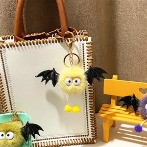 Detail of a cute yellow plush monster bat keychain with wings on a white stylish bag