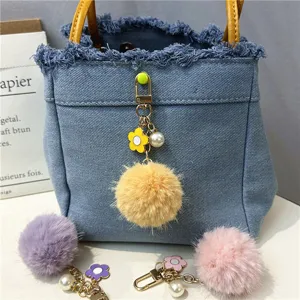 Detail view of colorful pom-pom charms with flower and pearl accents on denim bag