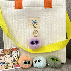 Cute fuzzy monster keychain charms with sunglasses and pearls on a bag.