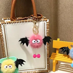 Detail view of a cute pink plush monster keychain with black bat wings on a white bag.