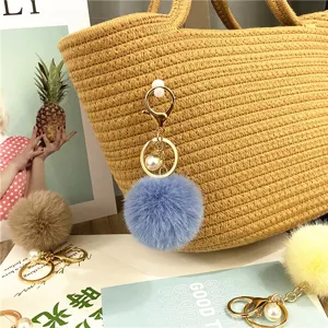 Close-up of blue plush ball keychain with gold ring and pearl charm on straw bag.