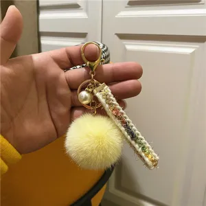 Close-up of yellow pom-pom keychain with tweed strap and pearl decoration